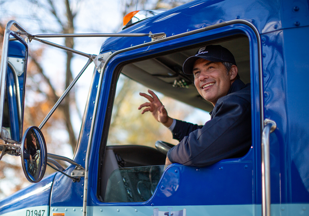 A Ferrellgas Delivery Driver smiles and waves from inside a propane delivery truck.