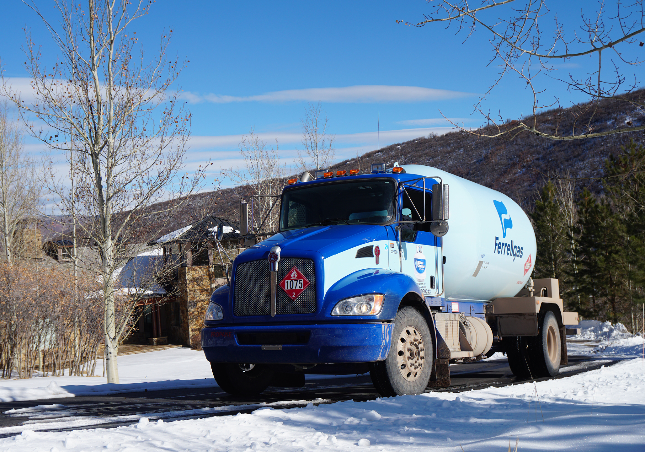 Propane truck delivering to a home with snow cleared around tank area.