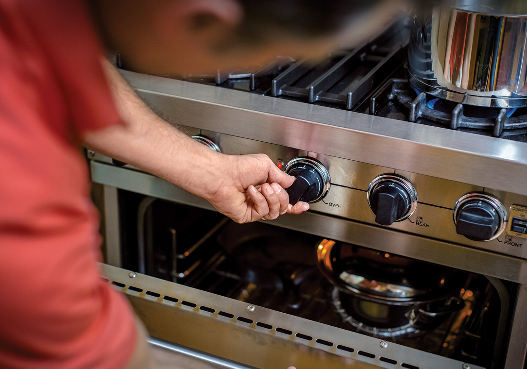 Close-up image of a man turning on a propane-powered cooking range.