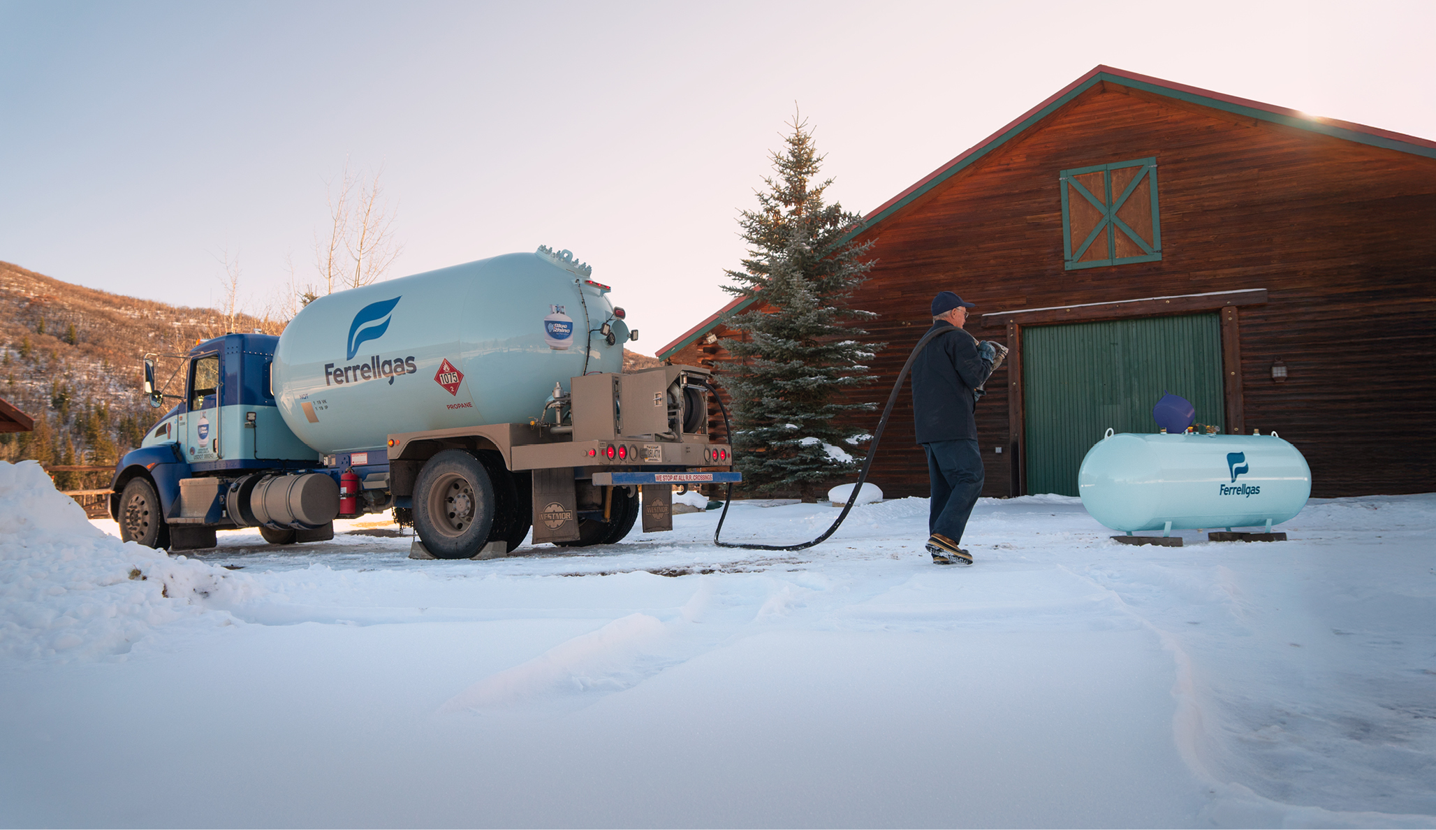 Ferrellgas delivery driver pulling a hose from the delivery truck to a residential propane tank that sits in a snow-covered yard. 
