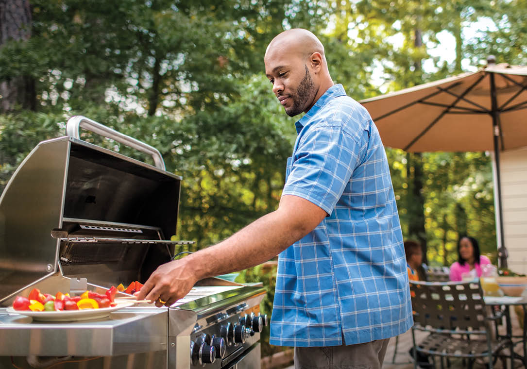 A man is cooking vegetables on a gas grill.